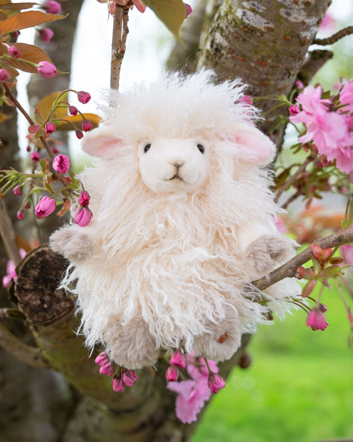 Ein super flauschiges Beryl Schaf Kuscheltier von Wrendale Designs sitzt in einem Baum zwischen den Kirschblüten.