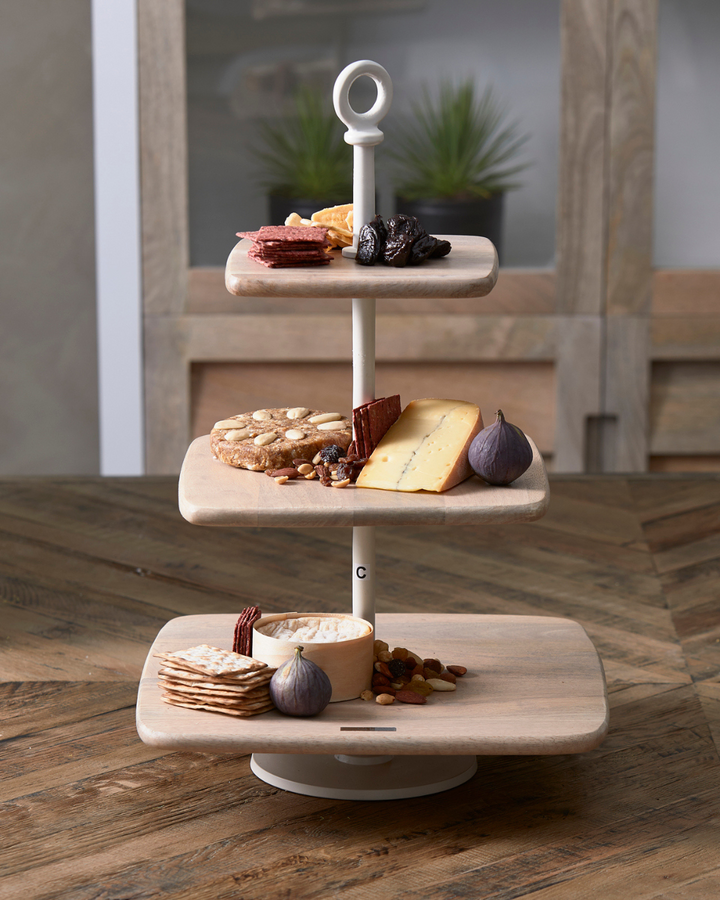 Die Côte Des Basques Etagère von Rivièra Maison ist auf einem Holztisch mit verschiedenem Essen dekoriert.