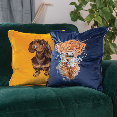 Kombination des gelben Dackel Kissens mit dem dunkelblauen Hochland Kuh Kissens von Wrendale Designs auf einer dunkelgrünen Couch.