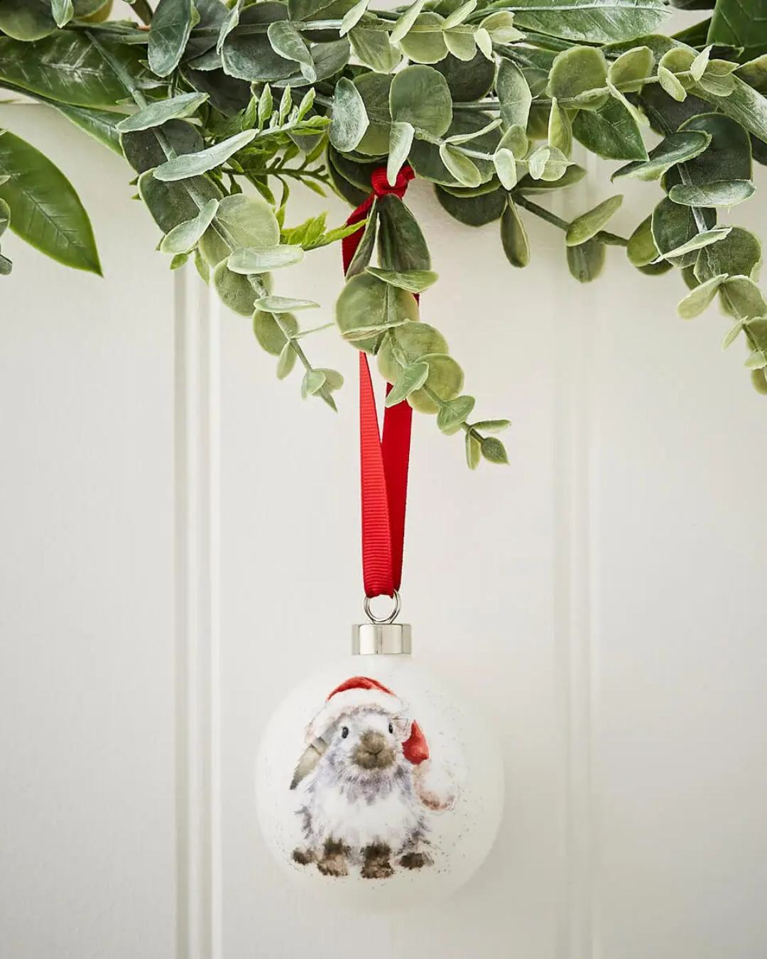Weiße Porzellankugel von Wrendale Designs mit Kaninchenmotiv und Weihnachtsmütze hängend.
