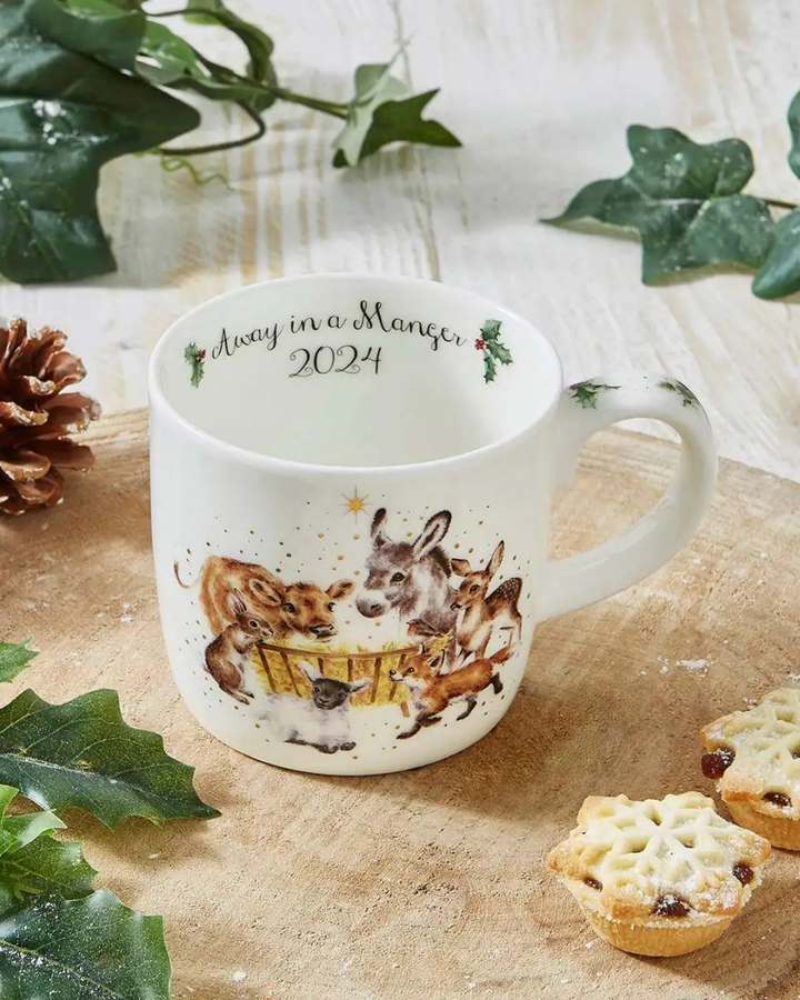Dekorierte Szene mit der Krippentier-Tasse von Wrendale Designs auf einem Holztisch mit Gebäck und Wintergrün.