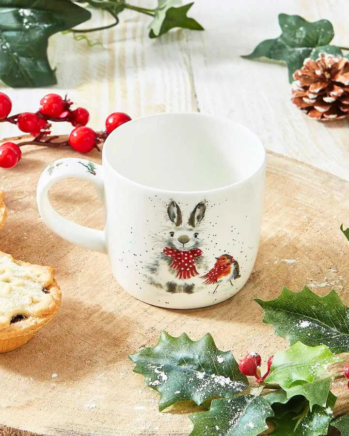 Dekorierte Szene mit der Schneetiere-Tasse von Wrendale Designs auf einem Holztisch mit Gebäck und Wintergrün.