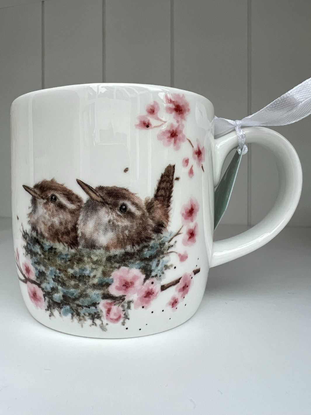 Die Feather your Nest Tasse von Wrendale Designs zeigt zwei Vogelküken in ihrem Nest im Kirschbaum.