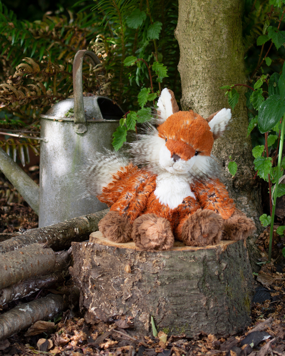 Das Fuchs Kuscheltier Autumn von Wrendale Designs sitzt im Wald auf einem Baumstumpf.