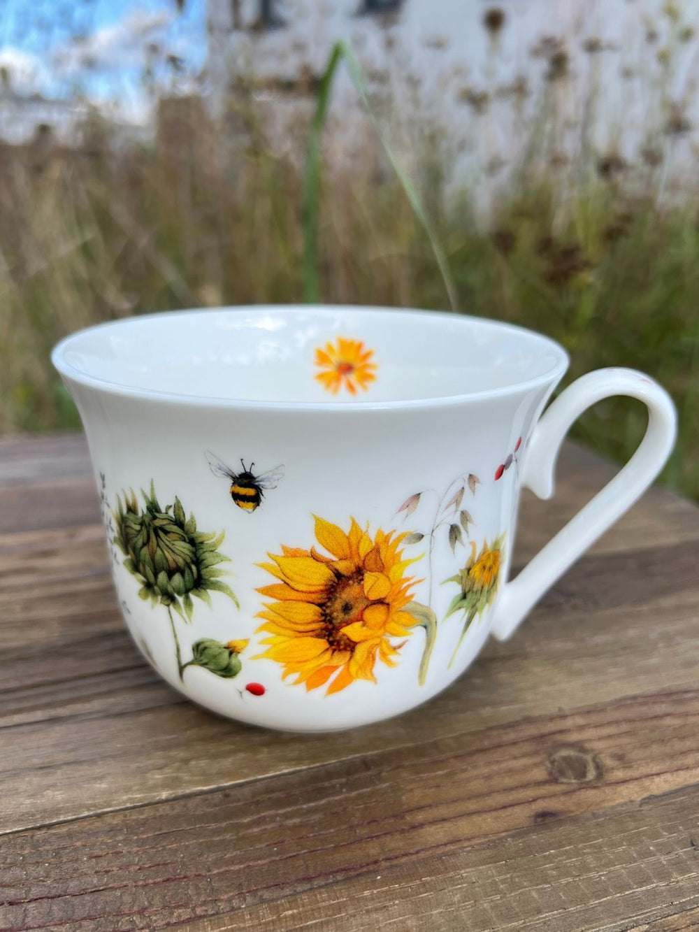 Vorderseite der Grätz Verlag Lieblingstasse mit Sonnenblumen auf einem Holztisch in der grünen Wiese.