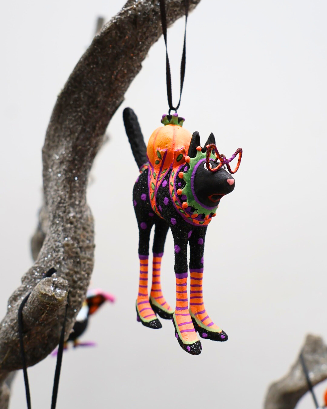 An einem Ast hängende Krinkle Katze Mini Back Cat von Patience Brewster.