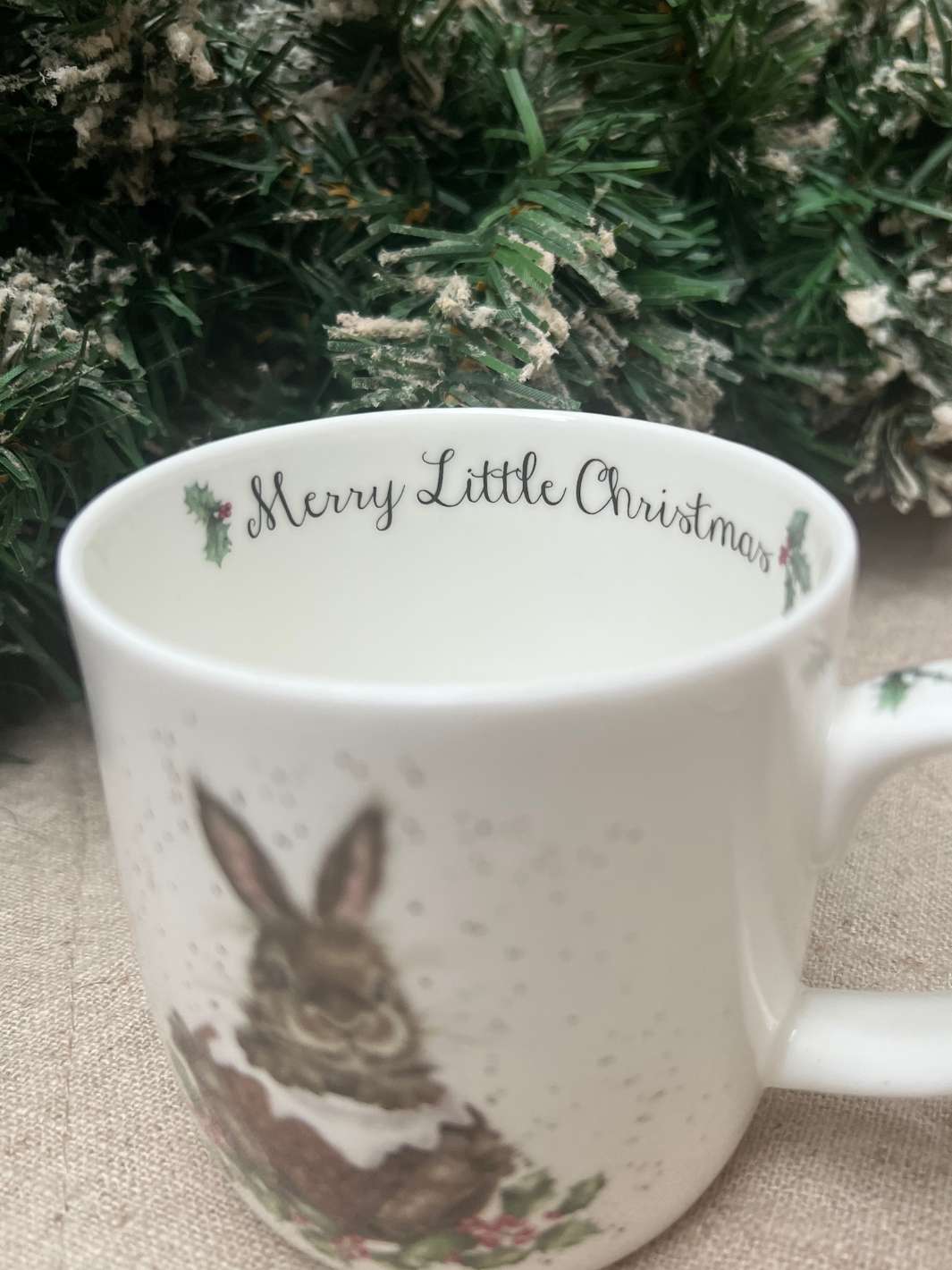 Innenansicht der Hasen Tasse von Wrendale Designs mit der Schrift Merry Little Christmas vor weihnachtlichem Hintergrund.