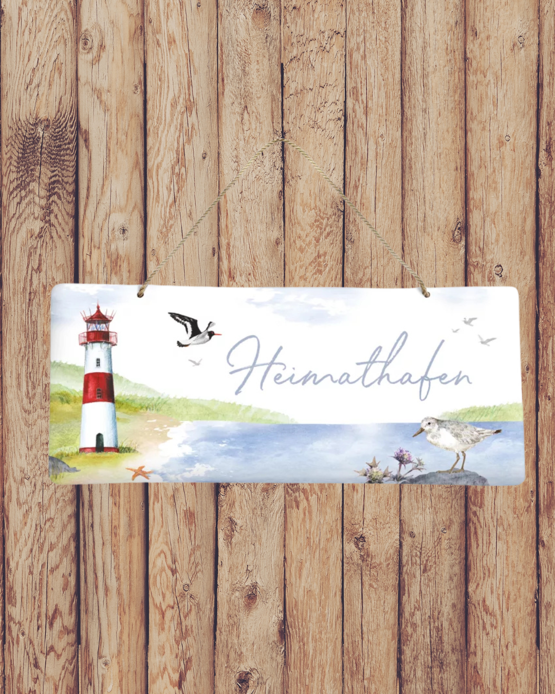 Süßes Metallschild Heimathafen vom Grätz Verlag vor Holzwand dekoriert, mit Möwen, Meer und Leuchtturm als Motiv.