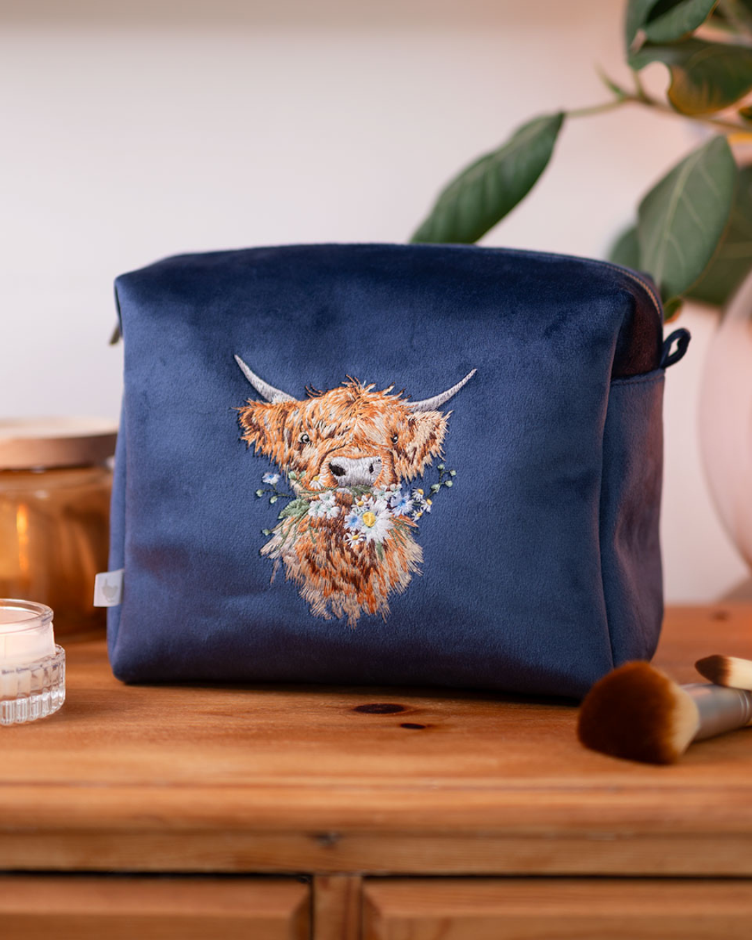 Große dunkelblaue Kosmetiktasche mit gesticktem Hochlandrind von Wrendale Designs, dekorativ auf einem Holztisch platziert.