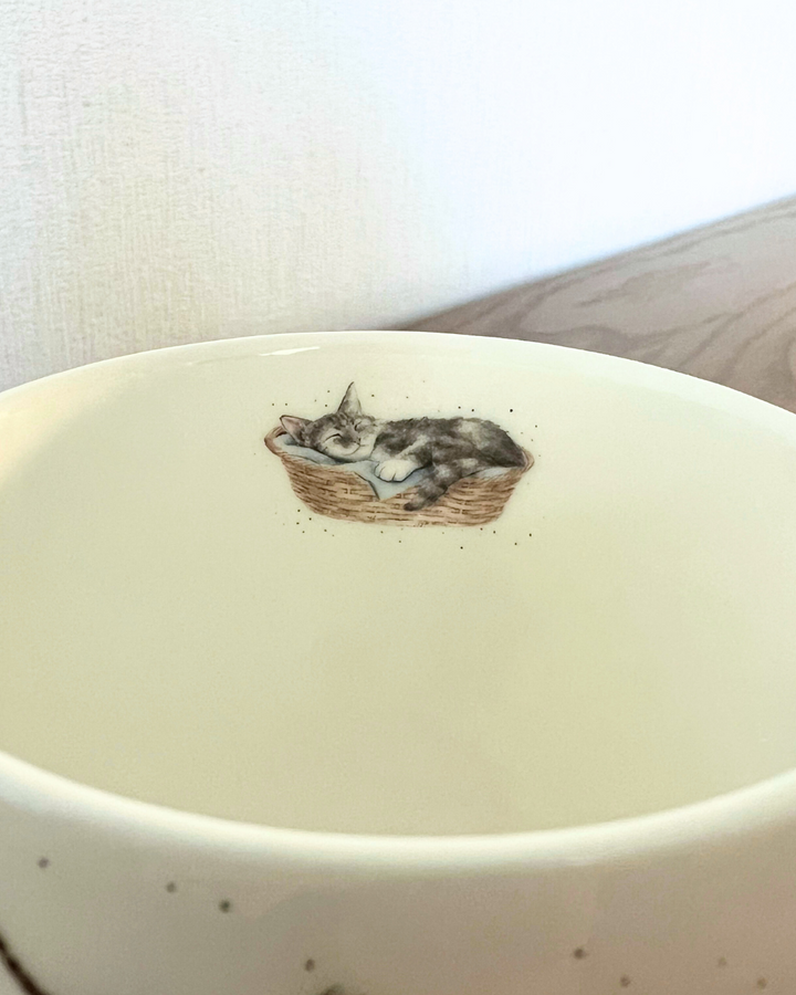 Das Innenmotiv der Katzen Tasse Cattitude von Wrendale Designs zeigt eine in einem Körbchen schlafende Katze.