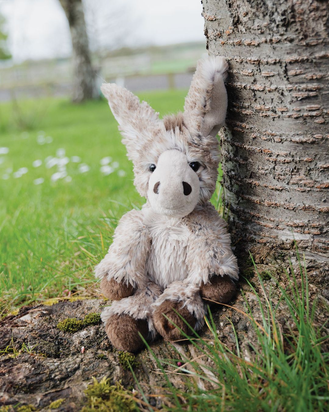 Jack das kleine Esel Kuscheltier von Wrendale Designs in der Größe M sitzt ganz flauschig unter einem Baum.