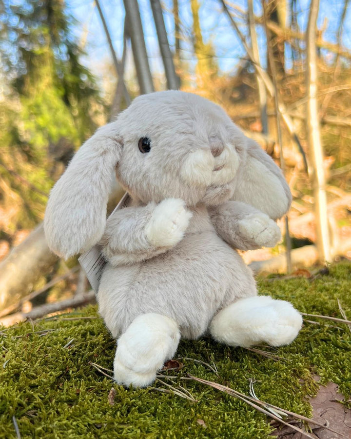 Kaninchen Kuscheltier Kanini in pastell blau von Bukowski sitzt auf einem Baumstamm.