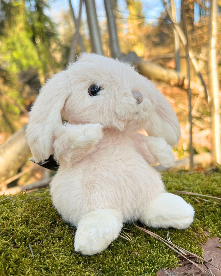 Kaninchen Kuscheltier Kanini in pastell rosa von Bukowski sitzt auf einem Baumstamm.