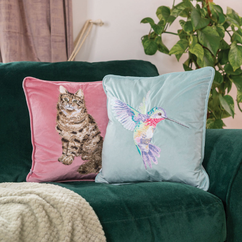 Kombination des rosa Katzen Kissens mit dem türkisen Kolibri Kissens von Wrendale Designs auf einer dunkelgrünen Couch.