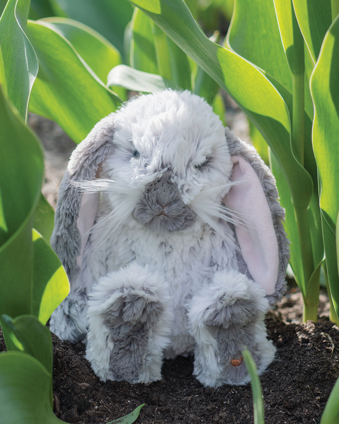 Das kleines Rosie Hasen kuscheltier von Wrendale Designs sitzt vergnügt zwischen Maiglöckchen.