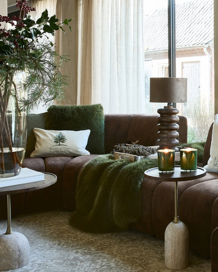 Wohnzimmer mit braunem Sofa, grünen Faux-Fur-Kissen und passenden Accessoires von Rivièra Maison