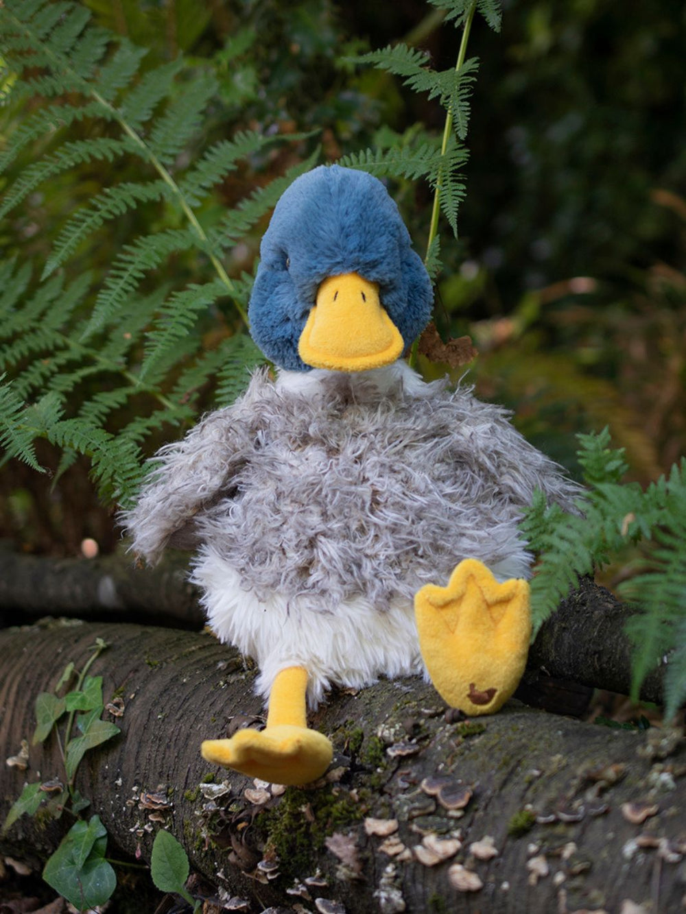 Die Kuscheltier Ente Webster von Wrendale Designs sitzt zwischen Farnen im Wald.