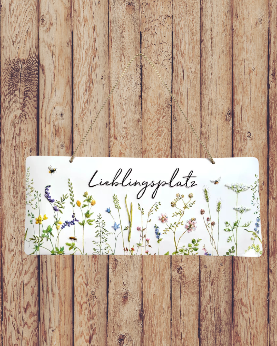 Süßes Metallschild ‚Lieblingsplatz‘ vom Grätz Verlag vor Holzwand dekoriert, mit Blumen und Bienen als Motiv.