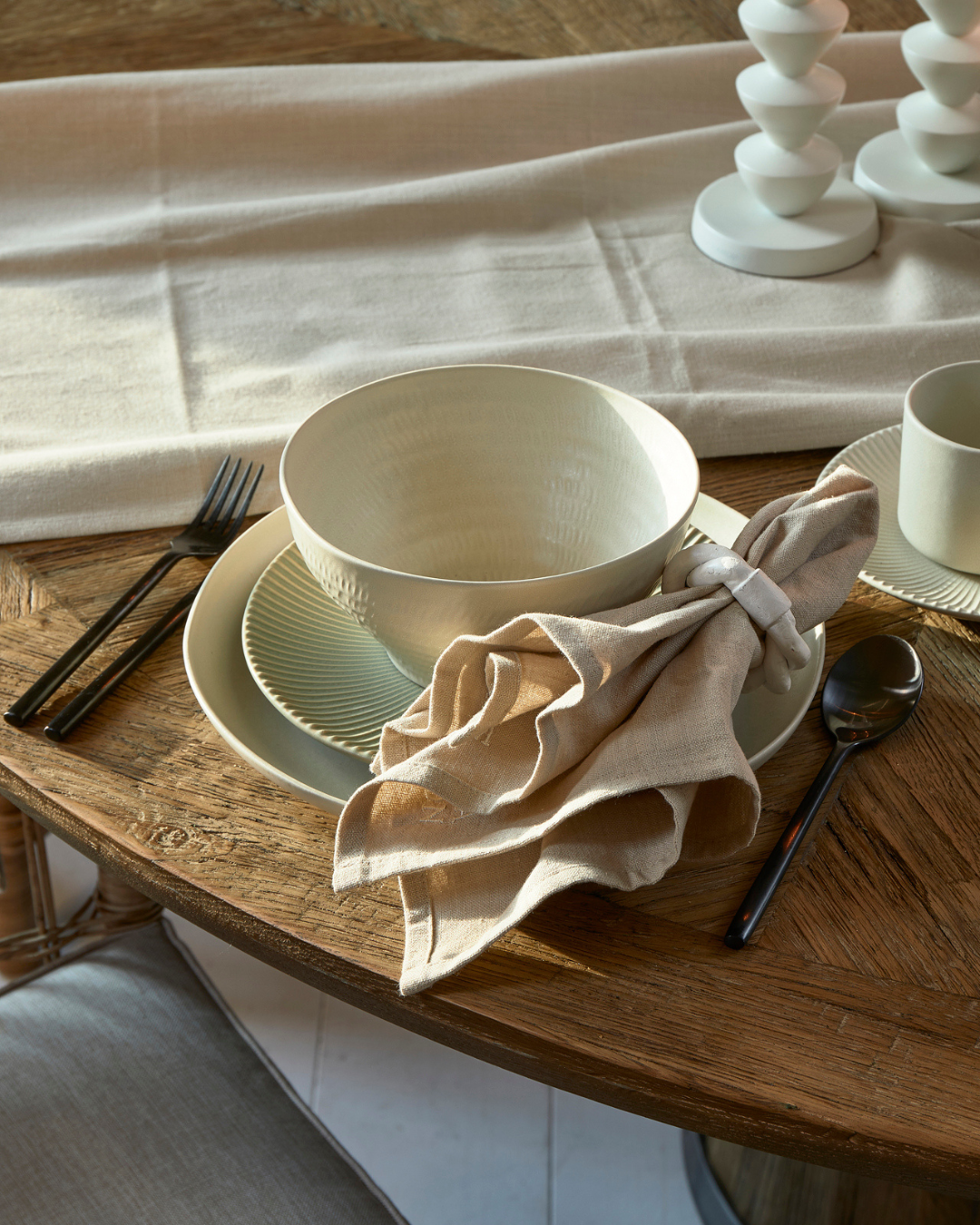 Kombination des Marseille Geschirrs von Rivièra Maison auf einem braunen runden Esstisch mit flaxfarbener Serviette daneben.
