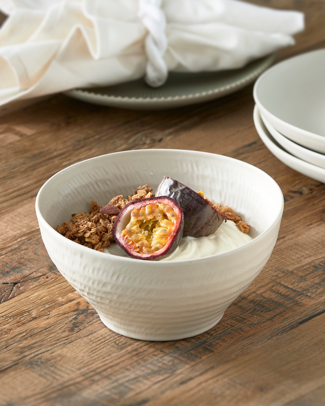 Weiße Marseille Schüssel von Rivièra Maison aus Keramik, mit feiner Struktur und zeitlosem Design. Auf einem rustikalen Holztisch serviert, gefüllt mit cremigem Joghurt, knusprigem Granola und frischer Passionsfrucht – elegantes Geschirr für Frühstück oder Dessert.