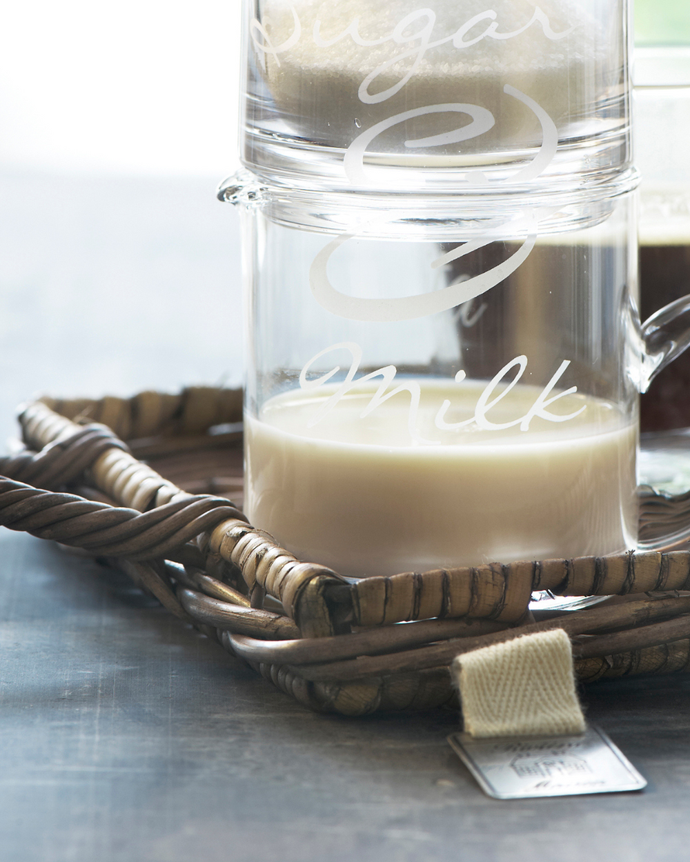 Nahaufnahme des Mini Tabletts aus Rattan von Rivièra Maison mit Milch- und Zuckerkännchen darauf.