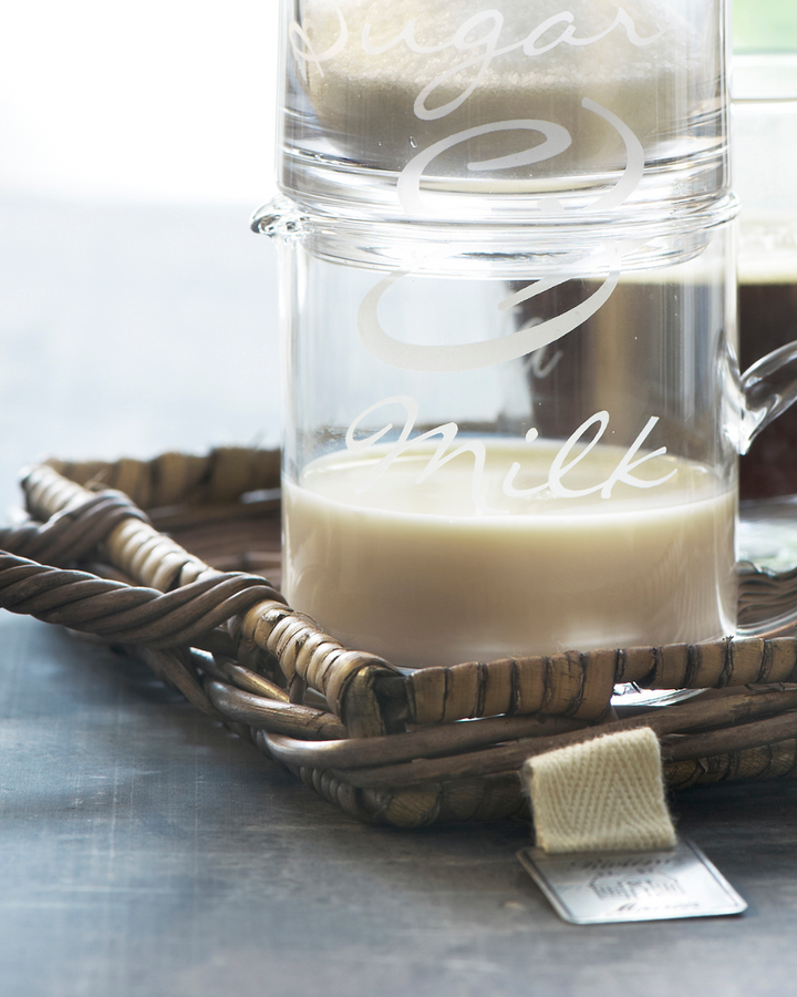 Nahaufnahme des Mini Tabletts aus Rattan von Rivièra Maison mit Milch- und Zuckerkännchen darauf.