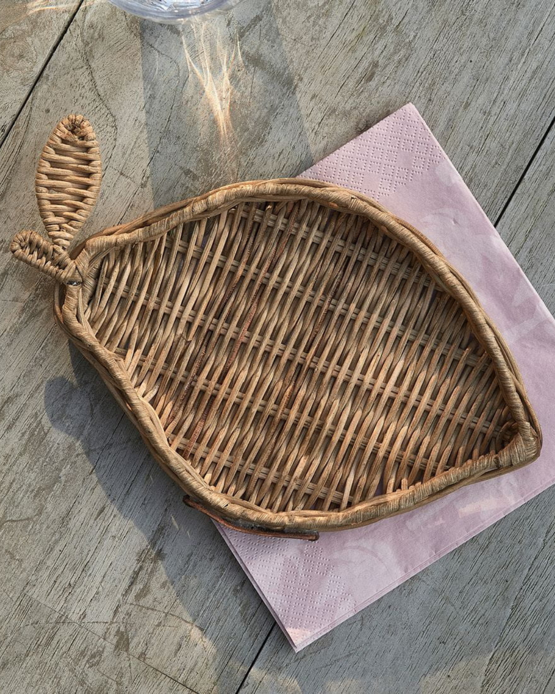 Das Rattan Zitronen Tablett von Rivièra Maison ist zusammen mit einer pinken Serviette auf einem braunen Holztisch dekoriert.