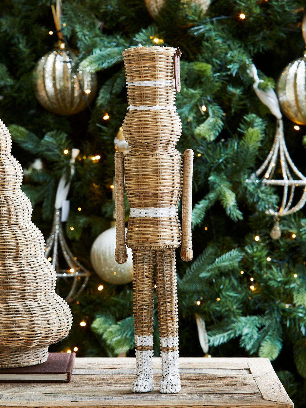 Weihnachtsdeko Rustic Rattan Nussknacker Statue von Rivièra Maison vor einem festlich geschmücktem Baum.