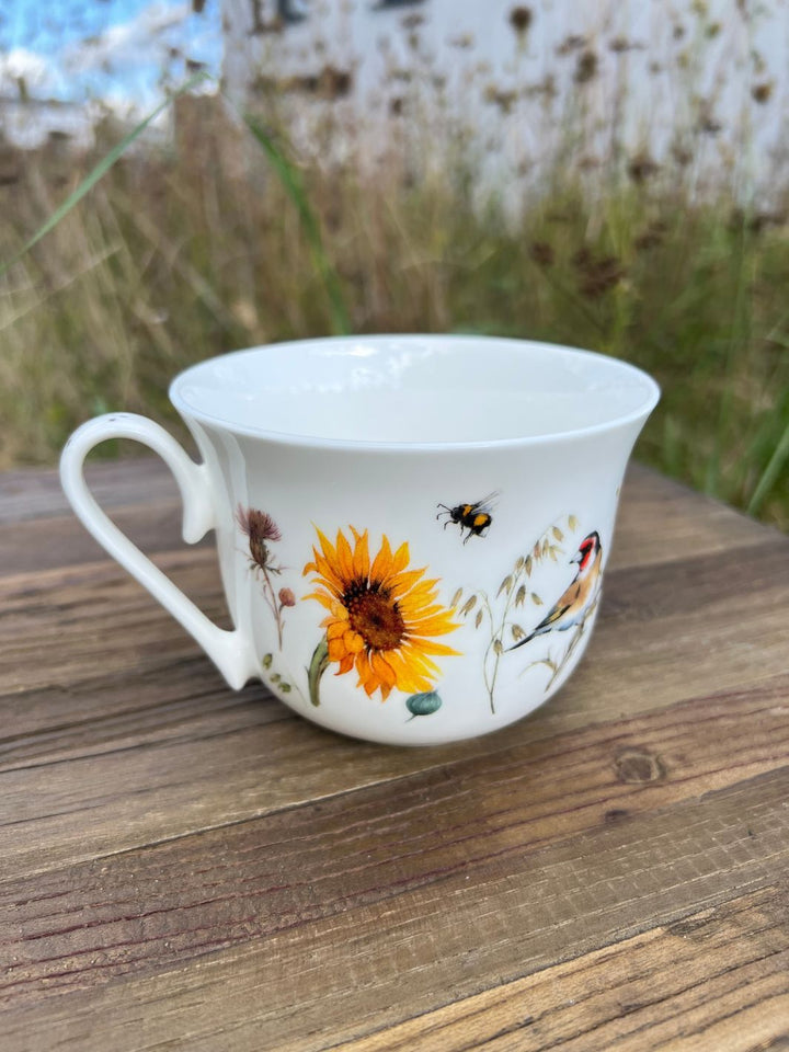 Rückseite der Lieblingstasse mit dem Sonnenblumen und Vogel-Motiv vom Grätz Verlag auf einem Holztisch in der grünen Herbstwiese.