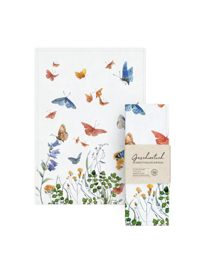 Geschirrtuch „Schmetterlingswiese“ vom Grätz Verlag mit Verpackung vor weißem Hintergrund. Das Motiv von Sophia Drescher zeigt sommerlichen Schmetterlingen und Blüten.
