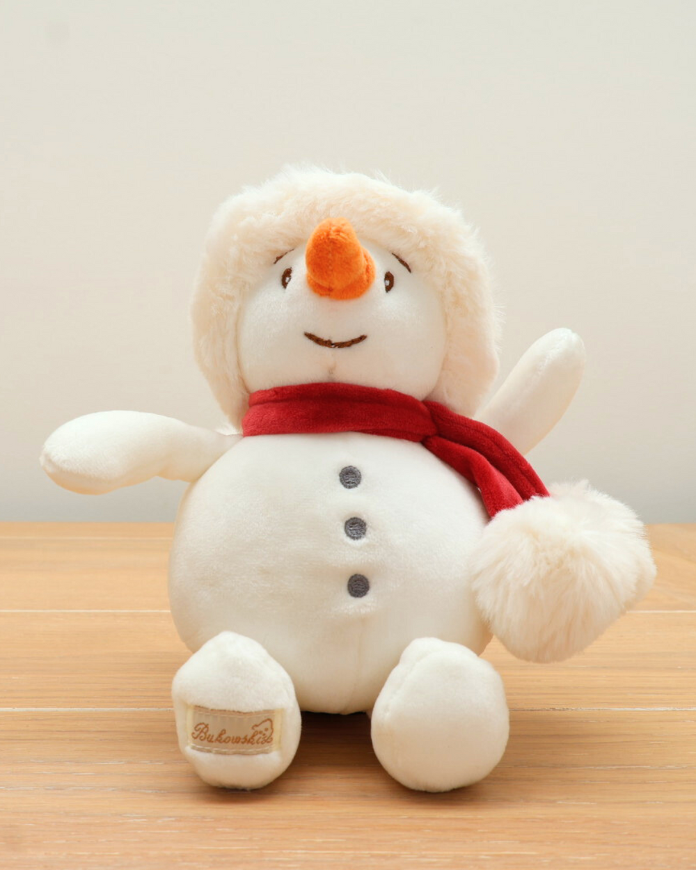 Das Baby Snowman Kuscheltier von Bukowski sitzend auf einem Holztisch.