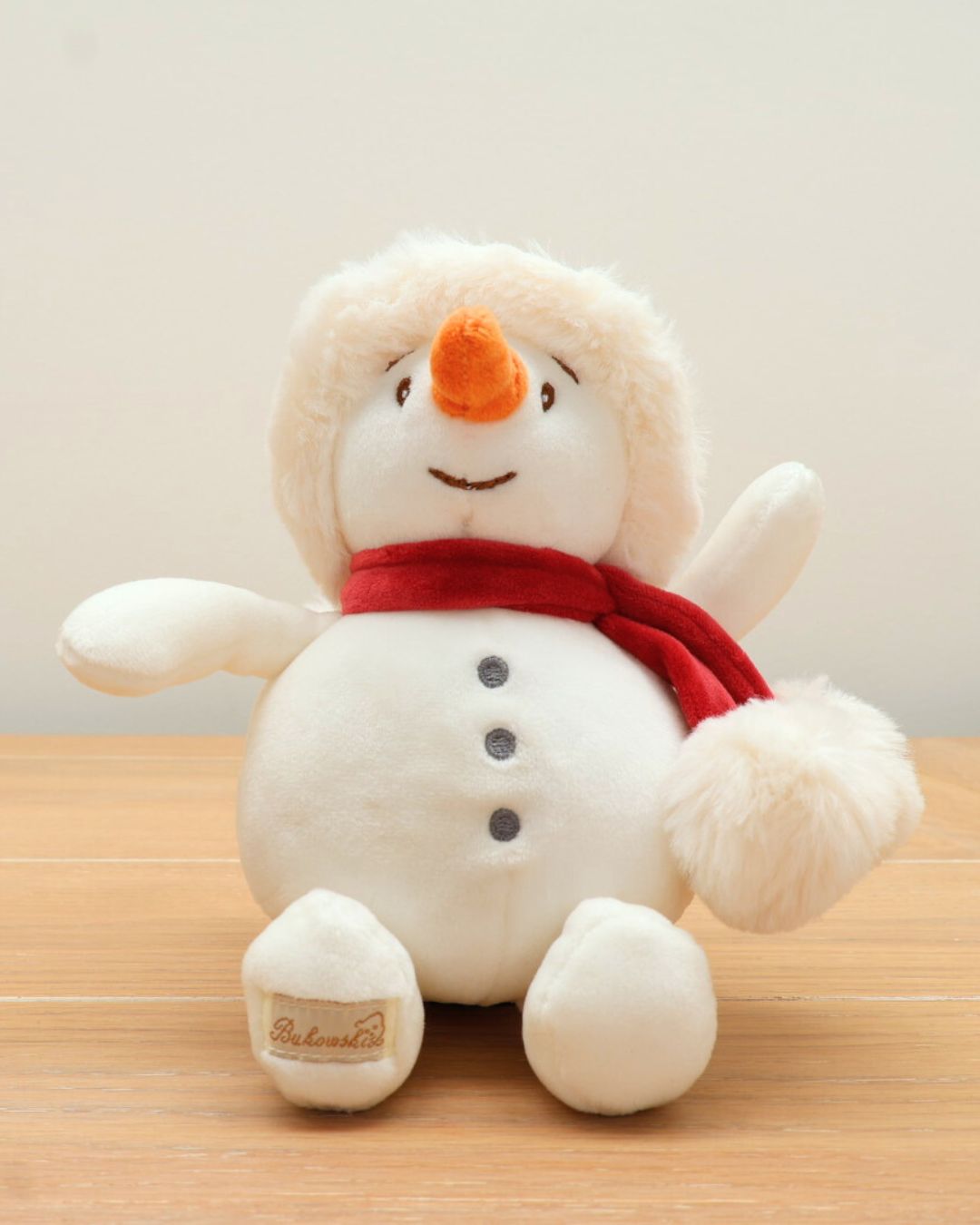 Das Baby Snowman Kuscheltier von Bukowski sitzend auf einem Holztisch.