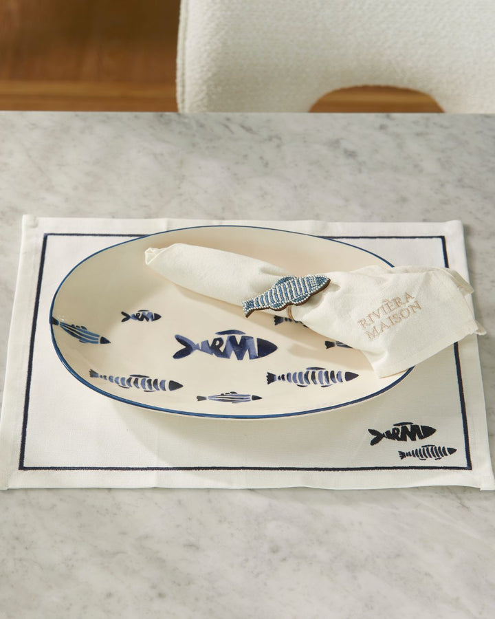 Servierplatte auf dem passenden Tischset aus der Como Catch Serie von Rivièra Maison mit Fisch Motiven drauf.