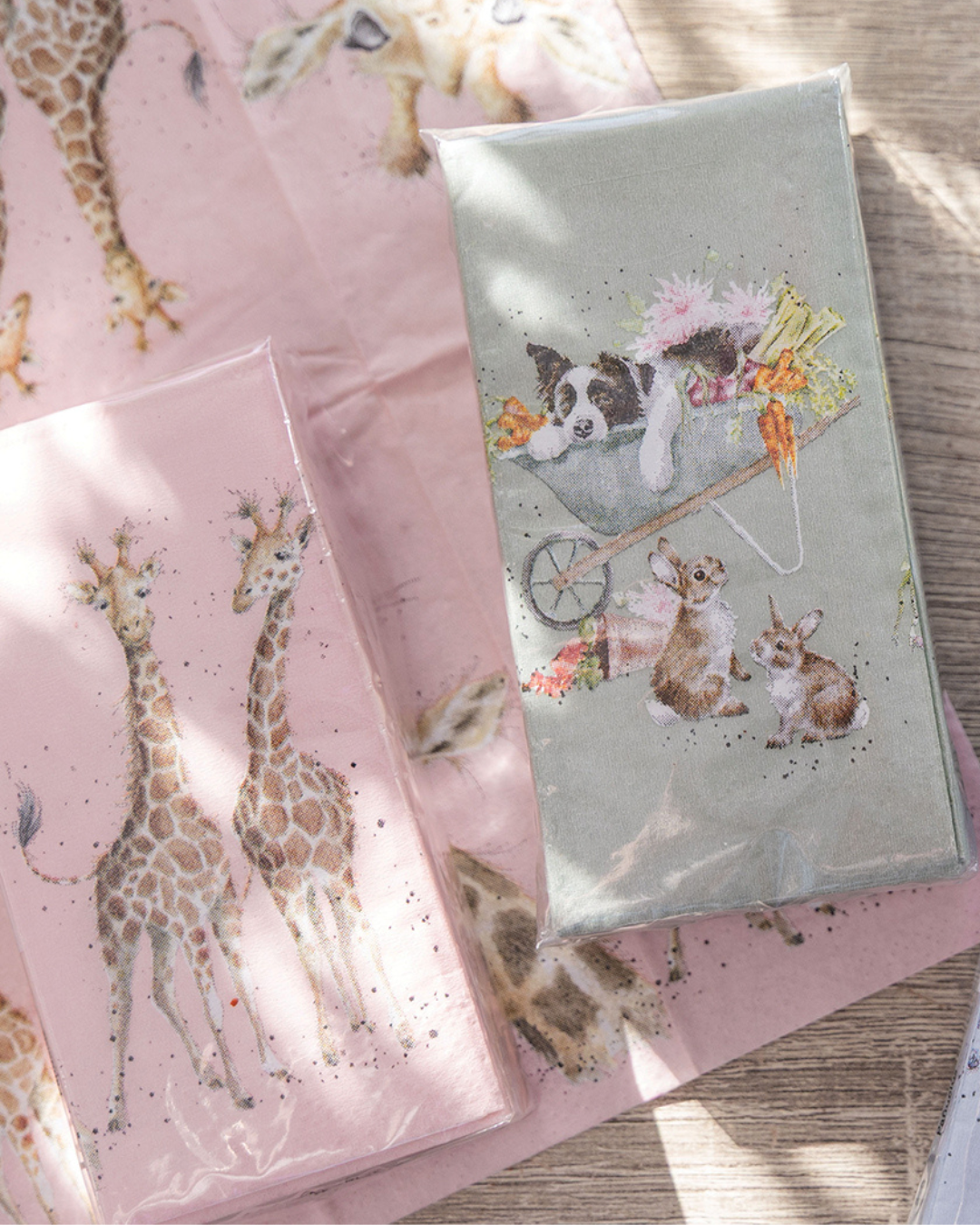 Giraffen- und Gartentiere-Taschentücher von Wrendale Designs nebeneinander liegend auf rosa Untergrund.