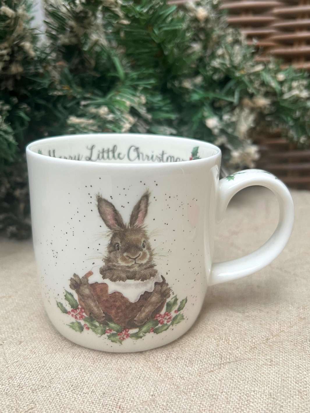 Winterliche Tasse von Wrendale Designs mit einem Hasen im Schnee vor einem weihnachtlichen Hintergrund.