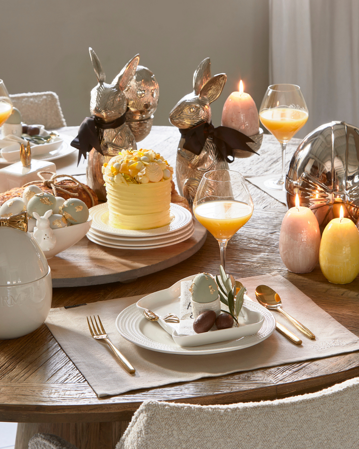Elegant gedeckter Tisch mit den RM Classic Placemat Platzsets von Rivièra Maison, dekoriert mit Tellern, Gläsern, goldfarbenem Besteck und Osterdekoration.