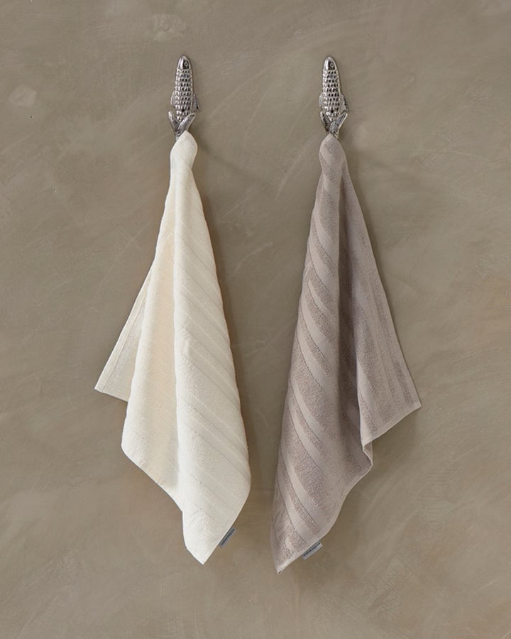 Zwei Ubuntu Küchenhandtücher von Rivièra Maison, in Beige und Weiß, dekorativ an Haken aufgehängt.