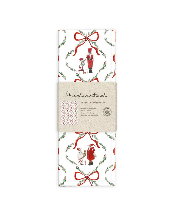 Verpacktes Geschirrtuch Weihnachtswerkstatt vom Grätz Verlag vor weißem Hintergrund. Die Vorderseite zeigt eine Detailansicht der Illustration von Silke Leffler mit Weihnachtsfiguren.