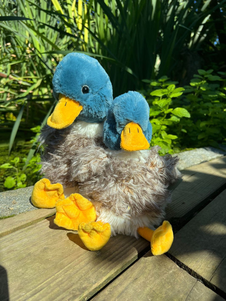 Die Wrendale Designs Kuscheltier Enten Webster in den Farben blau, grau,weiß und gelb sitzen am Teich.
