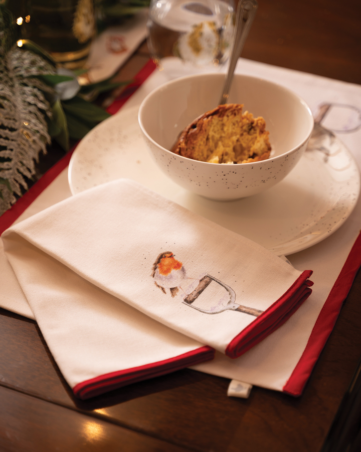 Das Tischset „Winter Woodland“ von Wrendale Designs mit Rotkehlchen-Motiv auf einem Spatenstiel. Es liegt auf einem festlich dekorierten Tisch mit Schale, Besteck und winterlichem Grün – perfekt für eine stimmungsvolle Adventstafel.