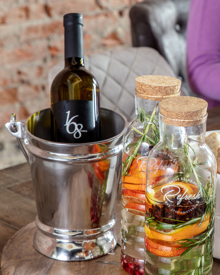 Fire Brigade Weinkühler von Rivièra Maison mit einer Weinflasche, daneben zwei Wasserkaraffen mit Zitrusfrüchten und Rosmarin auf einem Holztisch.