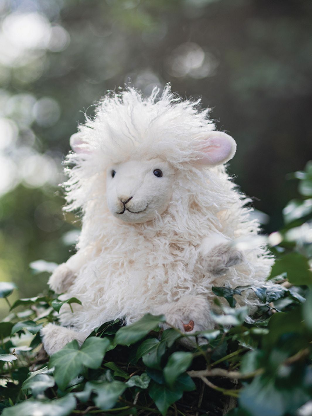 Wrendale Designs Kuscheltier Beryl Schaf sitzt auf einem Baumstamm mit Efeu und sieht einfach niedlich aus.