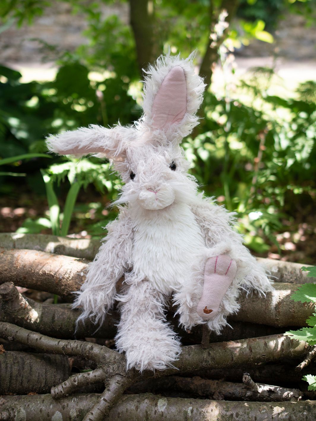 Der Wrendale Designs Kuscheltier Hase Rowan in den Farben grau und weiß sitzt im Wald.