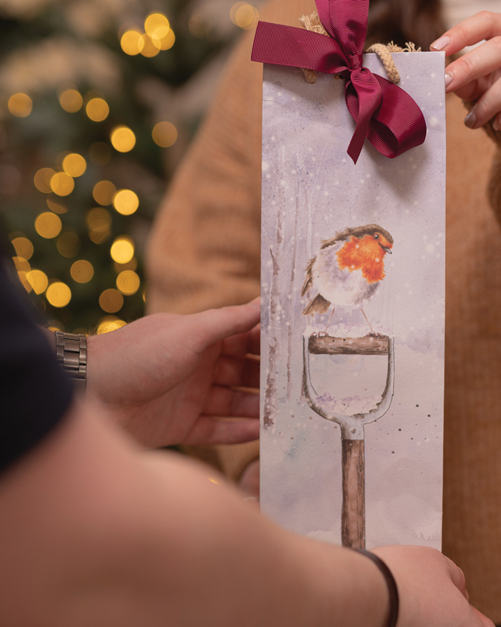Geschenkübergabe mit Flaschen-Geschenktasche „A Little Red Robin“ von Wrendale Designs.