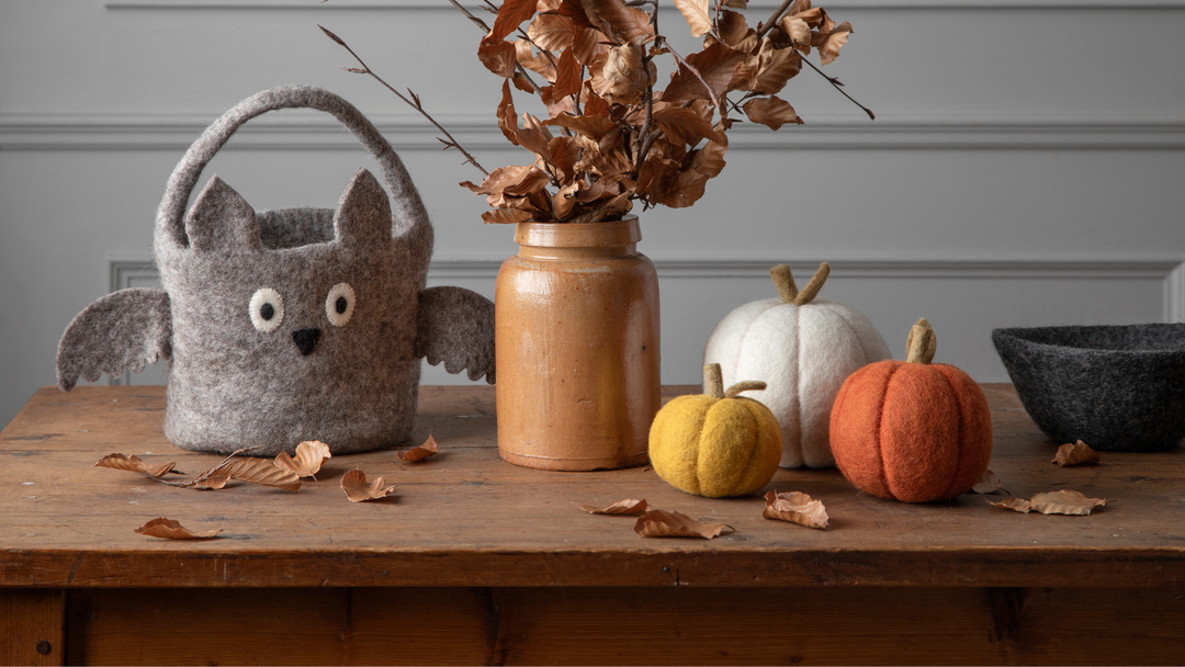 Herbstliches Ambiente mit trockenen Ästen in einer Vase, Filzkürbissen in weiß, orange und gelb, sowie einem Halloween Trick or Treat Körbchen aus grauem Filz in Form einer Fledermaus von Gry & Sif.