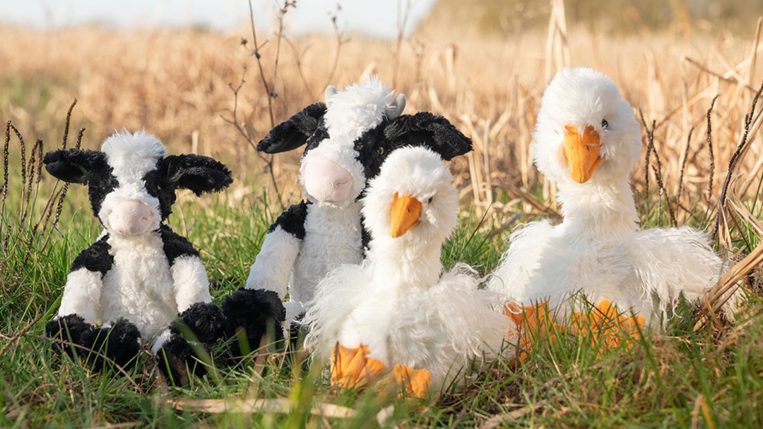 Neue Kuscheltiere Kuh Mathilda und Gans Pearl in zwei Größen von Wrendale Designs dekoriert auf einer Wiese.