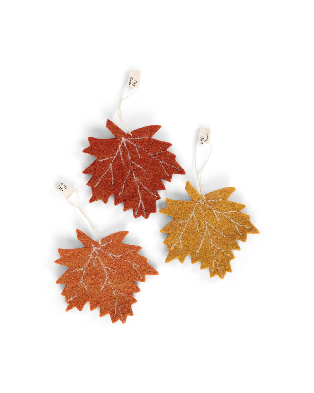 Drei herbstliche Filzanhänger in Ahornblatt-Form von Gry & Sif in Currygelb, Orange und Dunkelorange vor weißem Hintergund.