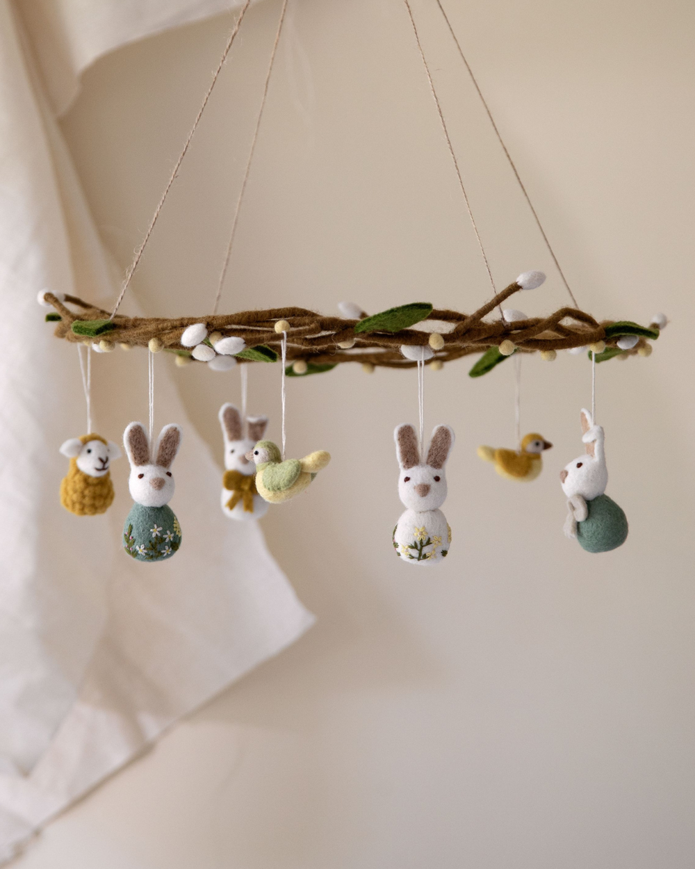 Filzkranz mit hängenden Schafen, Hasen und Vögeln von Gry & Sif, dekoriert mit Blättern und Knospen, aufgehängt vor hellem Stoffhintergrund.