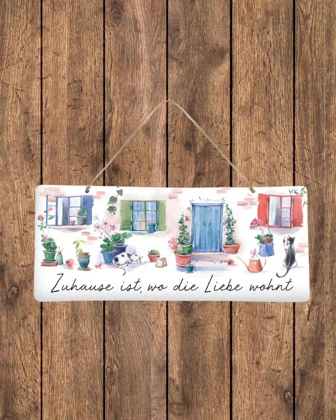 An einer Holzwand befestigtes Metallschild "Zeit zum Träumen" vom Grätz Verlag. Dieses ist mit dem Motiv einer Backsteinhausfassade bemalt. Drei bunte Fensterrahmen mit Gardinen und eine blaue Haustüre gehören zur Fassade. Mehrere Blumentöpfe mit unterschiedlichen Blühpflanzen stehen an der Fassade. Zwei süße Katzen sind ebenso in schlafender und spielender Position zu sehen.