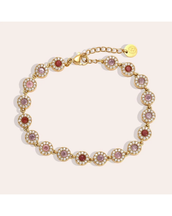 Armband mit bunten Glitzer Steinen von Dottilove vor beigen Hintergrund. Das Armband selbst ist Gold mit vielen Glitzer Steinen in rot, weiß und lila.